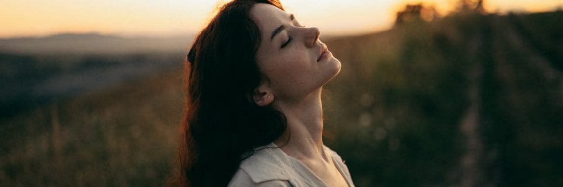 A serene woman with head tilted back, savoring the warm sunset in a field.